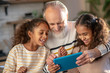 © zinkevych - Grey-haired bearded man and his granddaughters watching a video together and smiling