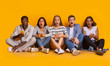 © Prostock-studio - Shocked teenagers using phones, sitting on floor over yellow background