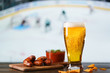 © Julia Fateyeva - Spicy barbecue chicken wings, tomato salsa, nachos and beer on dark wooden bar table. Hockey on background, high resolution