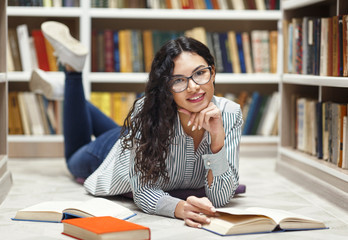 Wall Mural - Smiling latina girl reading books lying at library