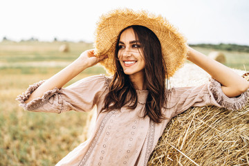 Closeup portrait of beautiful smiling woman with closed eyes. The brunette leaned on a bale of hay. A wheat field on the background