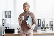 Smiling arabic woman in hijab with coffee and documents in office