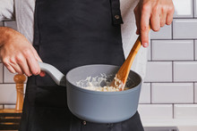 Man's Hands Close-up Holding A Saucepan And Stirring With Wooden Spoon.