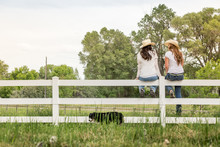 Two Western Girls Sitting On A Fence, Laughing. Bridger, Montana, USA