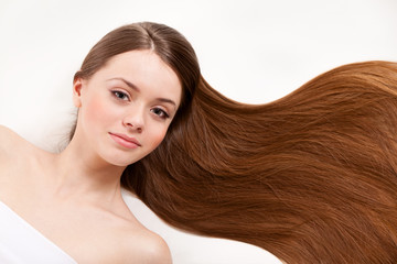 Beautiful woman lying on her back, with her long brown hair on white background, smiling and looking at camera