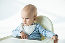 Pensive Baby Boy Sitting On Feeding Chair On White Background