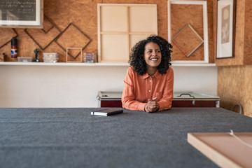 Wall Mural - Smiling woman sitting at a table in her framing studio