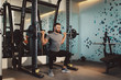 © djile - Young handsome man doing squat exercises at the gym on a squat machine
