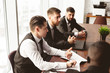 © xartproduction - A team of young businessmen in suits working and communicating together in an office. Corporate businessteam and manager in a meeting.