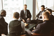 © xartproduction - A team of young businessmen in suits working and communicating together in an office. Corporate businessteam and manager in a meeting.