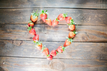 Wall Mural - frame from strawberry berries close up in the form of a heart on a wood   background