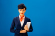 © LIGHTFIELD STUDIOS - smiling african american flight attendant holding digital tablet isolated on blue