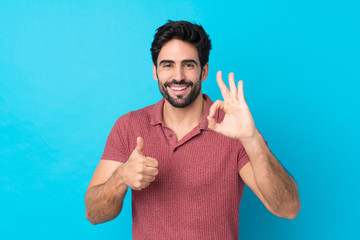 Wall Mural - Young handsome man with beard over isolated blue background showing ok sign and thumb up gesture