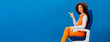 © LIGHTFIELD STUDIOS - panoramic shot of smiling african american in retro dress sitting on seat and pointing with finger isolated on blue