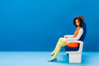 © LIGHTFIELD STUDIOS - african american in retro dress sitting on seat on blue background