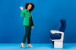 © LIGHTFIELD STUDIOS - smiling african american woman waving and standing near seats on blue background