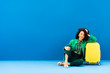 © LIGHTFIELD STUDIOS - smiling african american woman sitting near travel bag on blue background