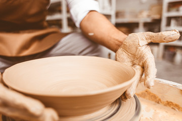 A young male potter works in his workshop on a potter's wheel and makes clay products. Close-up of hands