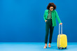 © LIGHTFIELD STUDIOS - smiling african american woman looking at travel bag on blue background