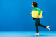© LIGHTFIELD STUDIOS - side view of smiling african american woman running with travel bag isolated on blue