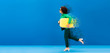 © LIGHTFIELD STUDIOS - panoramic shot of smiling african american woman running with travel bag on blue background