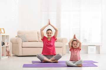 Wall Mural - Young mother with little daughter practicing yoga at home