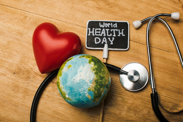 Wall Mural - Top view of decorative red heart, stethoscope, globe and card with world health day lettering on wooden background