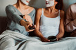 © lubero - .Group of friends applying a revitalizing white mask on their faces. Beauty treatment and skin care. Seated on the sofa drinking coffee and watching tv together. Close up