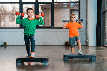 Front view of multicultural children holding dumbbells and doing Step Aerobics in gym