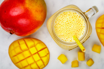 Wall Mural - Smoothie or milkshake made from fresh  mango, yogurt or milk and ice cubes in Mason jar on a marble table. Concept of healthy vitamin drinks. Selective focus, top view