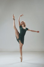Dancing Ballerina Stand On One Leg In Green Dress On Gray Background