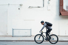 Side View Of Contemporary Male Cyclist In Black Helmet And Eyeglasses Surfing On Mobile Phone On White Wall Background