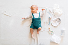 Top View Of Surprised Newborn Infant In Casual Wear Lying On Bed Near Toys Looking Away
