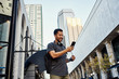 © Victor Bordera/ADDICTIVE STOCK - Contemporary Hispanic male tourist in casual wear and sunglasses with backpack and headphones using mobile phone at modern city street