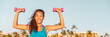 © Ariwasabi - Happy fitness Asian woman training shoulders with shoulder press dumbbells oudoor panoramic banner healthy active lifestyle. Girl lifting free weights in summer.