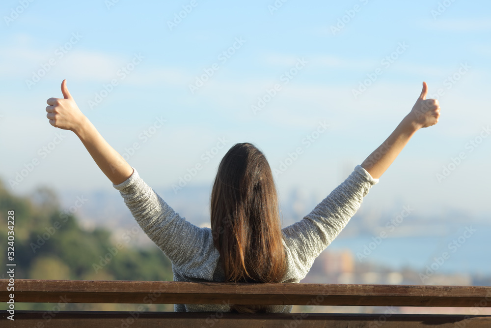 Woman raising hands with thumbs up sitting on a bench - obrazy, fototapety, plakaty 
