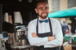 © Fxquadro - Handsome looking man barista working in a mobile coffee shop outdoors in the city emporium wearing apron and white shirt with bow tie, posing for the camera and smiling