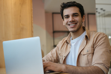 Asian student studying, learning language, online education concept. Portrait of handsome Indian businessman using laptop computer, working in office. Copywriter typing on keyboard, looking at camera