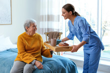 Care Worker Serving Dinner For Elderly Woman In Geriatric Hospice