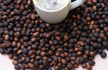 Cup of hot and creamy coffee and roasted coffee beans on the table