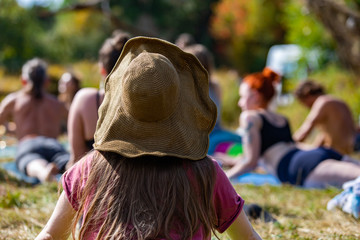 Poster - A close up view of a woman wearing a large brimmed hat, seen from behind, during a yoga exercise at a festival celebrating peace and earth, copy space to right