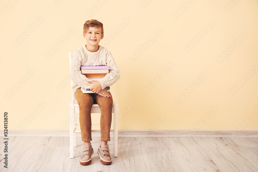 Little boy with books sitting near color wall