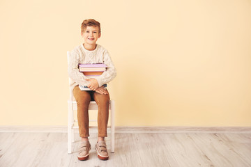 Wall Mural - Little boy with books sitting near color wall