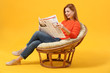 © Pixel-Shot - Beautiful woman reading newspaper while sitting in armchair against color background