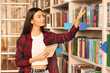 © Pixel-Shot - Young female student choosing book in library