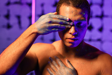 Wall Mural - Young African-American man with fluorescent paint on his skin on color background