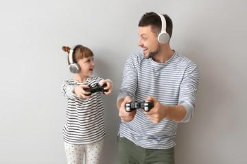Wall Mural - Father and his little daughter playing video games on grey background