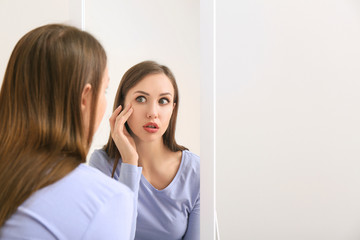 Shocked young woman looking in mirror at home