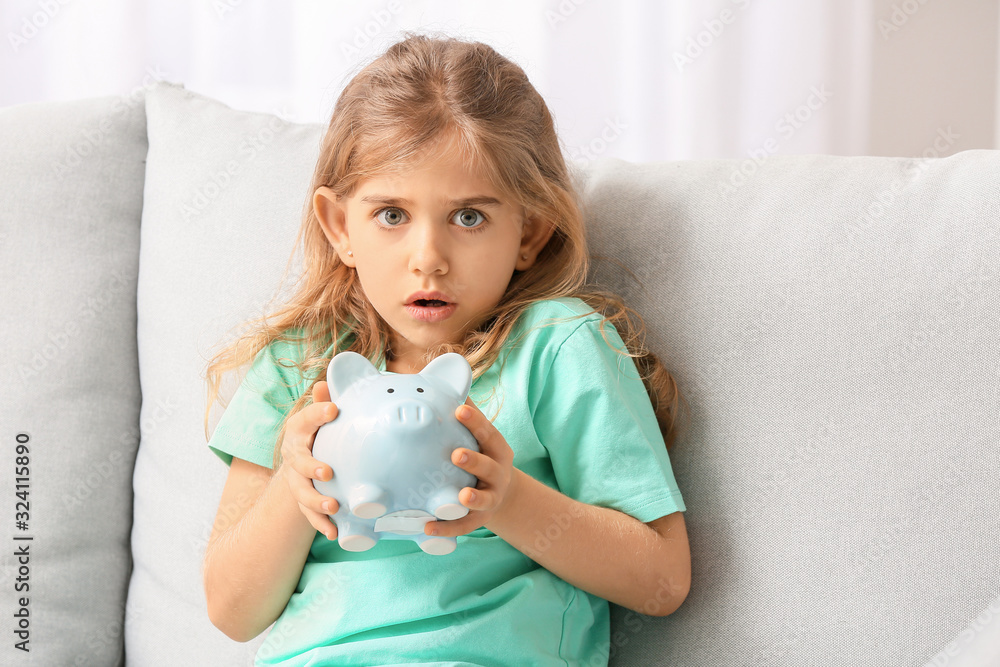 Scared cute girl with empty piggy bank at home
