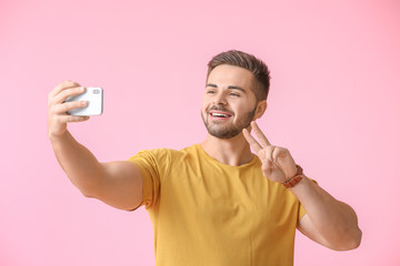 Wall Mural - Young man taking selfie on color background